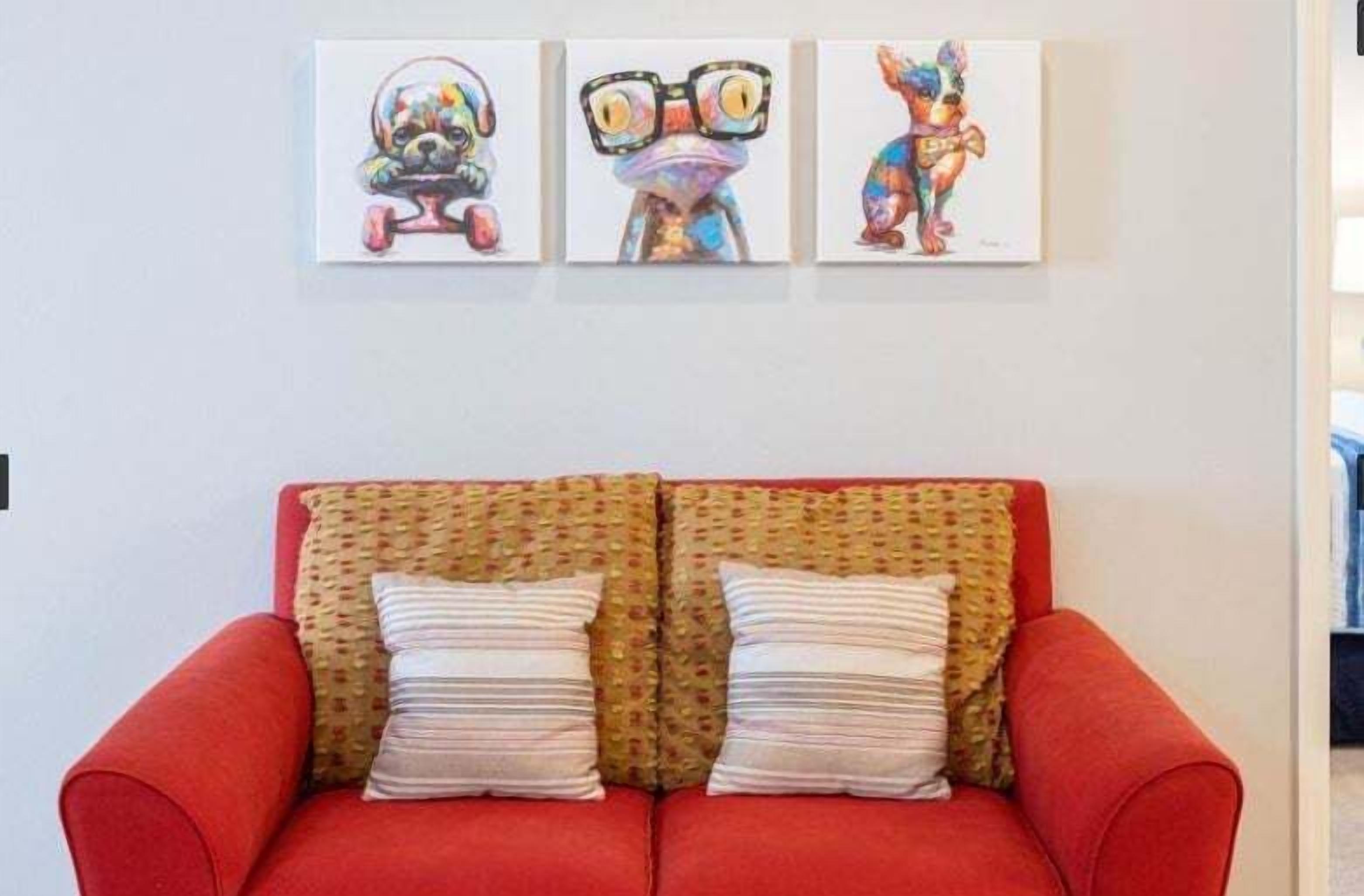A red sofa with two pillows, a wall with three framed artworks, and a woven headboard.