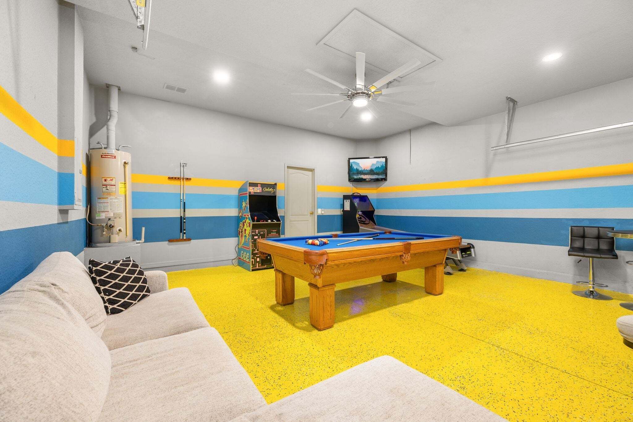 A pool table in a room with a ceiling fan, a television, and a sofa.