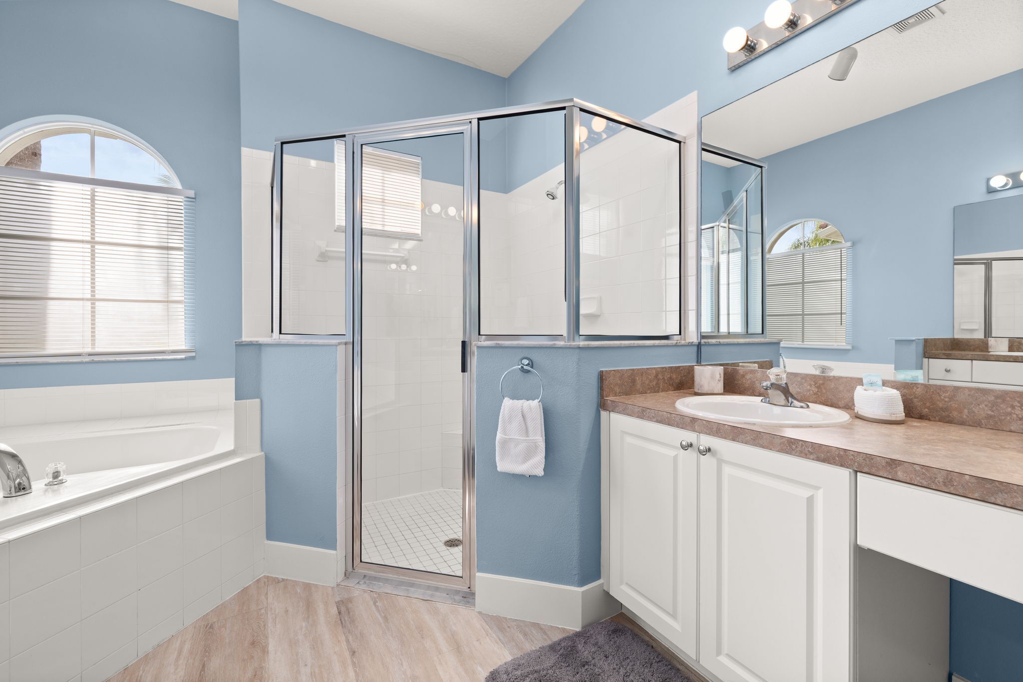 A modern bathroom with a glass shower enclosure, a bathtub, a sink with a vanity, and a large mirror.