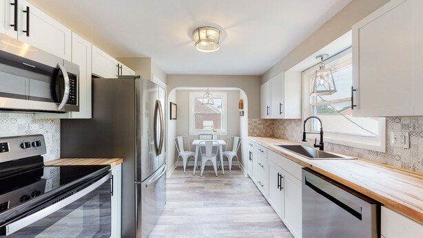 Una cocina moderna con electrodomésticos de acero inoxidable, armarios blancos y una zona de comedor con mesa y sillas.