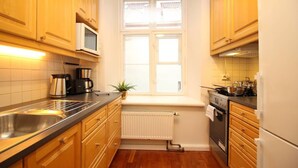 Une cuisine compacte avec des meubles en bois, un évier en acier inoxydable, une fenêtre avec vue, un radiateur et une cuisinière.