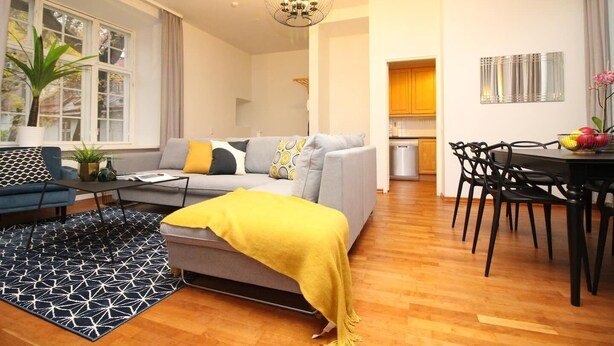 Un salon moderne avec un canapé gris, un plaid jaune et un coin repas avec des chaises noires.