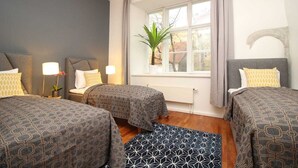Une chambre d’hôtel avec deux lits, une fenêtre avec des rideaux, un radiateur et une plante sur le rebord de la fenêtre.