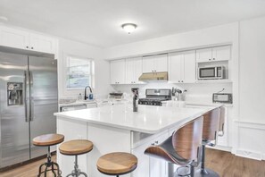 Una cocina moderna con armarios blancos, un refrigerador de acero inoxidable, un microondas y una isla central con taburetes.