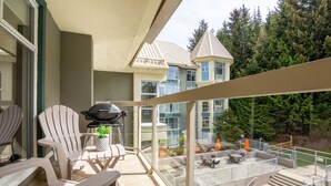 Un balcon avec des fauteuils Adirondack, un barbecue et une vue sur une maison dotée d’une tourelle.