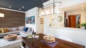 Un salon moderne avec un mur d’accent en bois, un coin repas doté d’une table en bois et une cuisine visible à travers une porte ouverte.