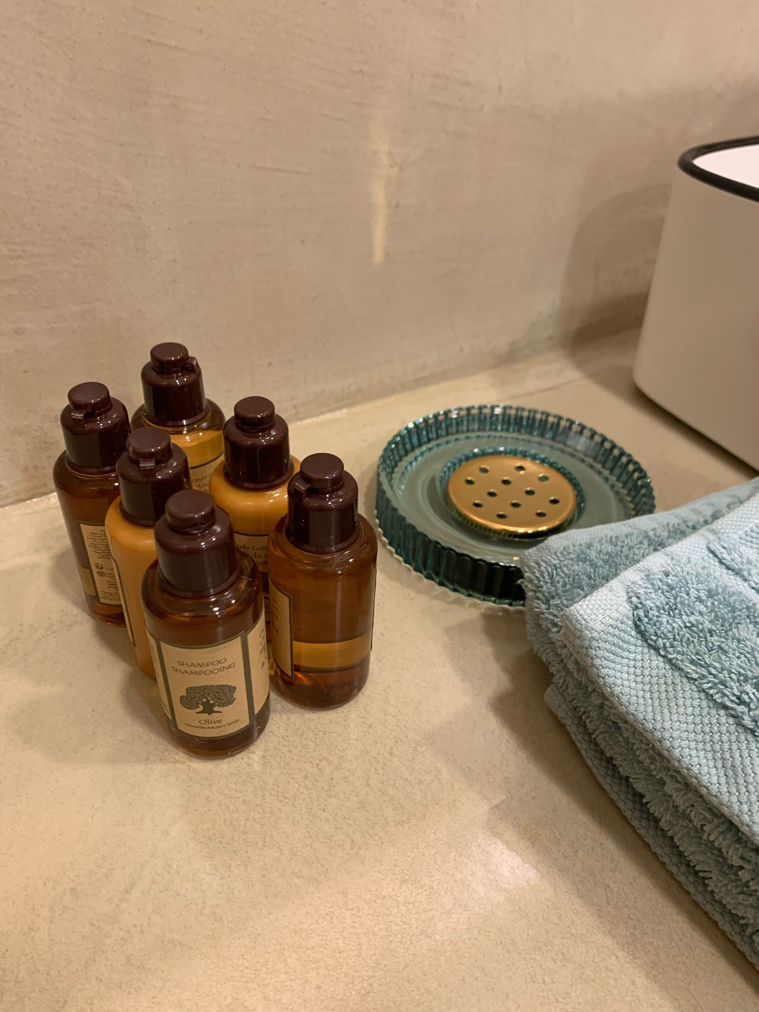 A bathroom counter with several bottles of shampoo, a green glass soap dish, and a folded towel.