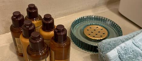 A bathroom counter with several bottles of shampoo, a green glass soap dish, and a folded towel.