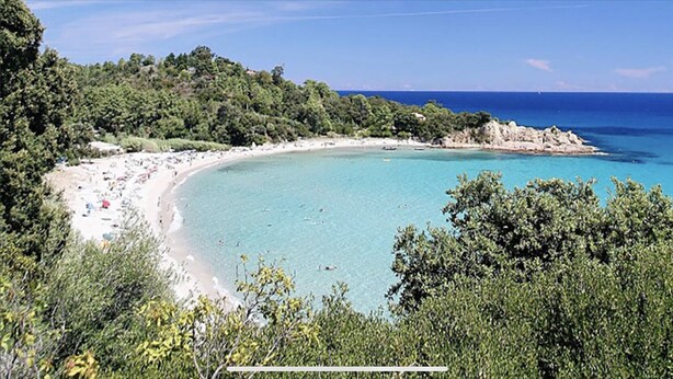 Una playa con aguas turquesas cristalinas, rodeada de abundante vegetación y afloramientos rocosos.