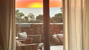 Habitación con vista al atardecer sobre el océano, con terraza de madera y zona de estar.