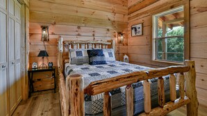 Ein Schlafzimmer einer Holzhütte mit einem Bett, Nachttischen und einem Fenster.