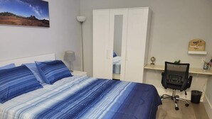 Et soveværelse med seng, garderobeskab, skrivebord og stol.