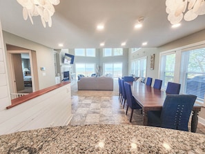 A spacious living area with a large dining table, comfortable seating, a fireplace, and a view of the ocean.