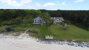 A coastal property with two large houses, a beach, and a forested area.