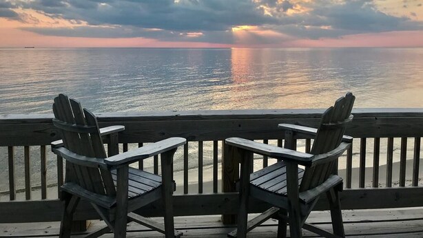 Un pontile in legno con due poltrone Adirondack rivolte verso un tramonto sull'acqua.