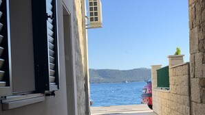 Uma trilha de pedra estreita leva a uma orla marítima, onde um carro está estacionado, com vista ampla para o mar.