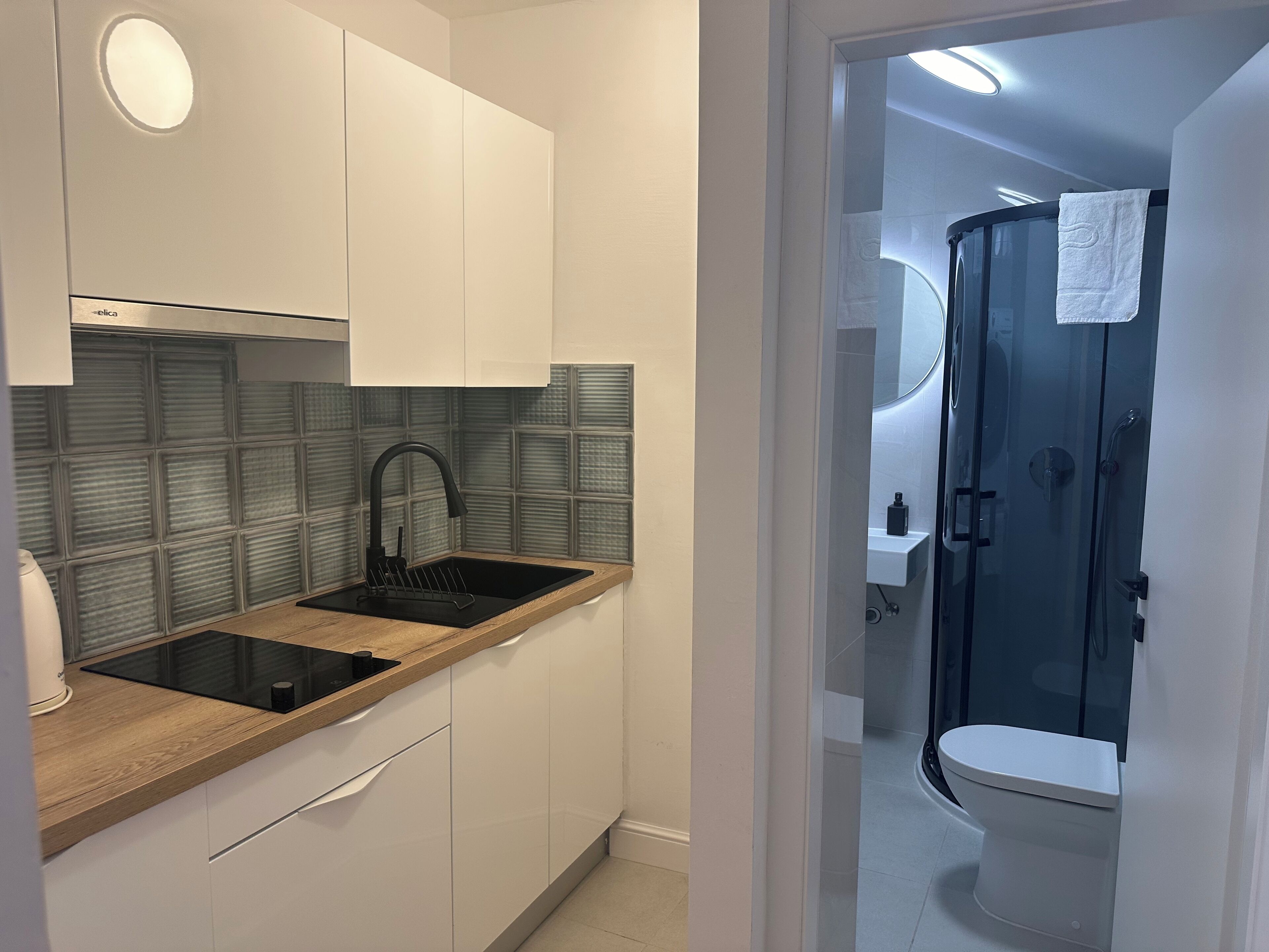 A compact kitchen with a black sink, wooden countertop, and white cabinets.