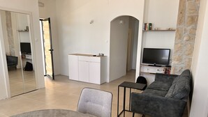En moderne stue med en grå sofa, et rundt bord med en plante, et hvidt skab og et TV monteret på en stenvæg.
