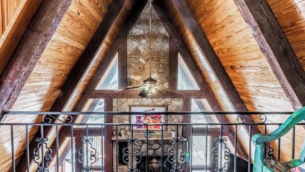 A wooden interior with a stone fireplace, a ceiling fan, and a metal railing.