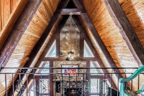 A wooden interior with a stone fireplace, a ceiling fan, and a metal railing. - Ruidoso Chalet: Hot Tub, Rock Views & Game Room (Ruidoso)
