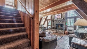 A wooden staircase leading to a living area with a stone fireplace, leather sofa, and a view of the outdoors.
