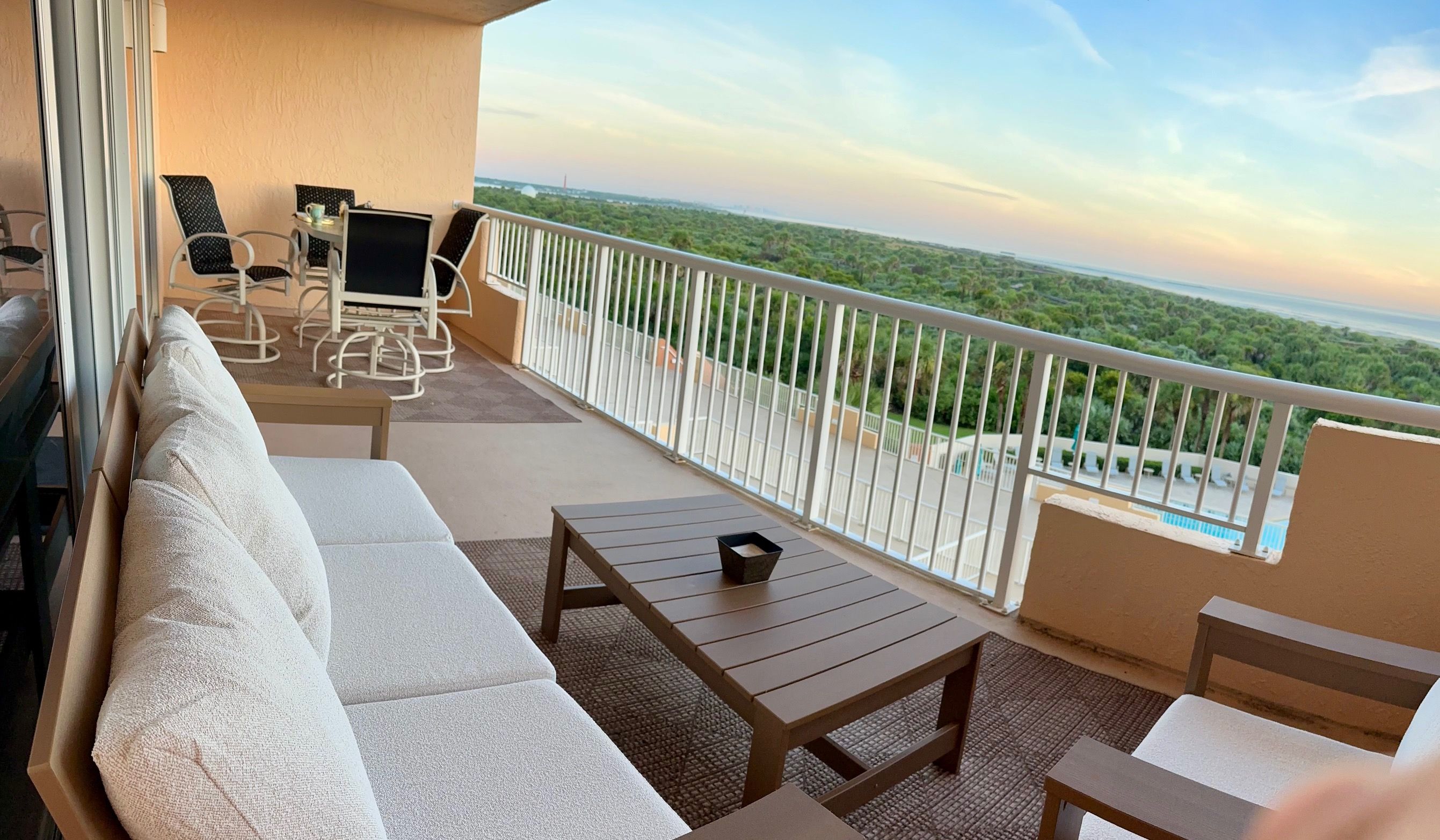 Ein Balkon mit einer Couch, Stühlen und einem Tisch, mit Blick auf eine üppige grüne Landschaft.