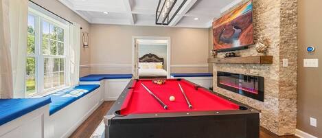 A pool table in a room with a stone wall, a fireplace, and a television.