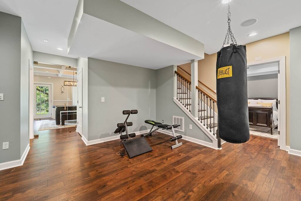 A spacious room with hardwood flooring, a punching bag, and a bench with dumbbells.