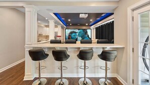 A modern kitchen with a central island, bar stools, and a large flat-screen TV.