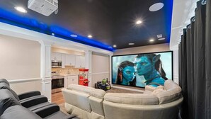 A home theater with a large flat-screen TV, a reclining sofa, and a ceiling-mounted projector.