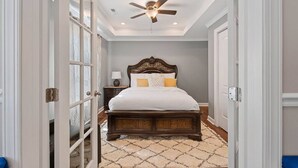 A bedroom with a large bed, a ceiling fan, and a patterned rug.