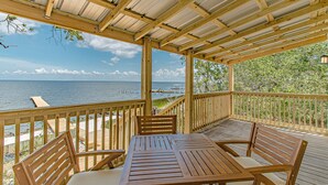 A covered outdoor area with a wooden table and chairs, overlooking a body of water and a pier. - Sunsets and Relaxation await -  Spot of Sun Bay Cottage (Gulf Shores)
