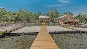 A wooden pier leading to a house with a balcony, surrounded by water and vegetation. - Sunsets and Relaxation await -  Spot of Sun Bay Cottage (Gulf Shores)