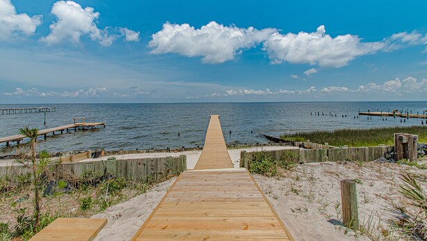 A wooden boardwalk leading to the water, surrounded by sandy areas and wooden fences. - Sunsets and Relaxation await -  Spot of Sun Bay Cottage (Gulf Shores)