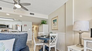 A modern kitchen with white cabinets, a microwave, and a refrigerator. There is a dining area with a round table and white chairs.