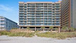 A multi-story hotel with balconies, a beach view, and a parking structure.