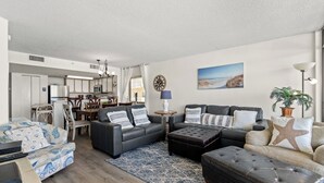 A modern living room with a sofa set, ottoman, and a dining area with chairs and a table.