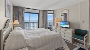 Une chambre d’hôtel avec un grand lit, une télévision, une commode et une vue sur l’océan.