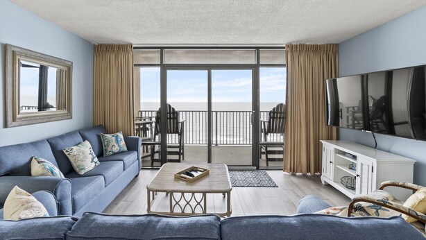 Un salon avec un canapé, une table basse, un téléviseur et un balcon offrant une vue agréable.