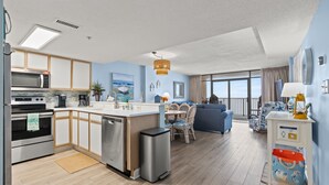 Une cuisine moderne équipée d’un four à micro-ondes, d’un four et d’un lave-vaisselle. Un coin repas avec une table et des chaises est également disponible. La pièce dispose d’une grande fenêtre offrant une vue sur le ciel.