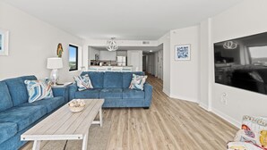 Ein modernes Wohnzimmer mit einem blauen Sofa, einem Holztisch und einer Küche im Hintergrund.