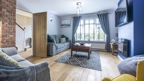A living room with a brick wall, a wooden door, a grey sofa, a coffee table, and a blue accent wall. - Mayfield House - 4 Bedroom House - Tenby (Tenby)
