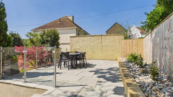 A patio with a table and chairs, a wooden fence, and a garden with pebbles and plants.