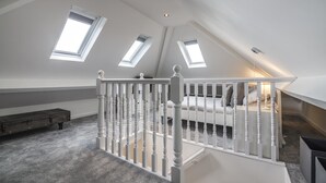 A spacious attic bedroom with a sloped ceiling, skylights, a white railing, and a bed with pillows. - Mayfield House - 4 Bedroom House - Tenby (Tenby)