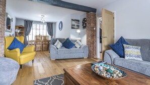 A living room with two sofas, a yellow armchair, and a coffee table with decorative items. - Mayfield House - 4 Bedroom House - Tenby (Tenby)