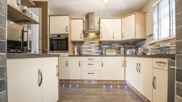 A modern kitchen with white cabinets, a Bosch oven, and a backsplash of gray tiles. - Mayfield House - 4 Bedroom House - Tenby (Tenby)