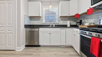 A modern kitchen with white cabinetry, a stainless steel dishwasher, a built-in oven, and a hanging pendant light.