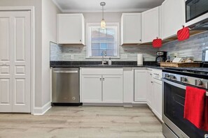 A modern kitchen with white cabinetry, a stainless steel dishwasher, a built-in oven, and a hanging pendant light.