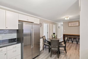 Une cuisine moderne avec des meubles blancs, un réfrigérateur en acier inoxydable et un coin repas comprenant une table ronde et des chaises.