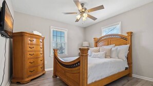 A bedroom with a wooden bed, a dresser, a ceiling fan, and two windows.